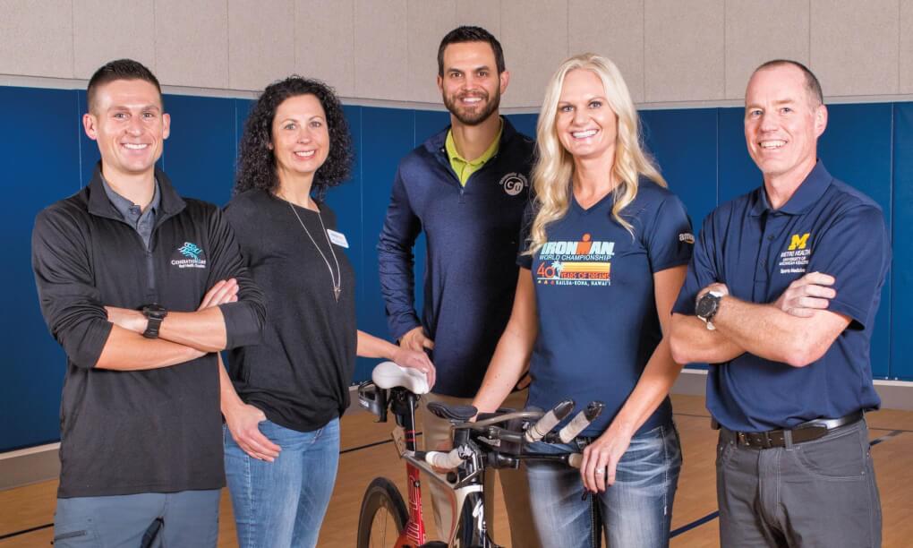Woman with bike stands with team of people in a gym
